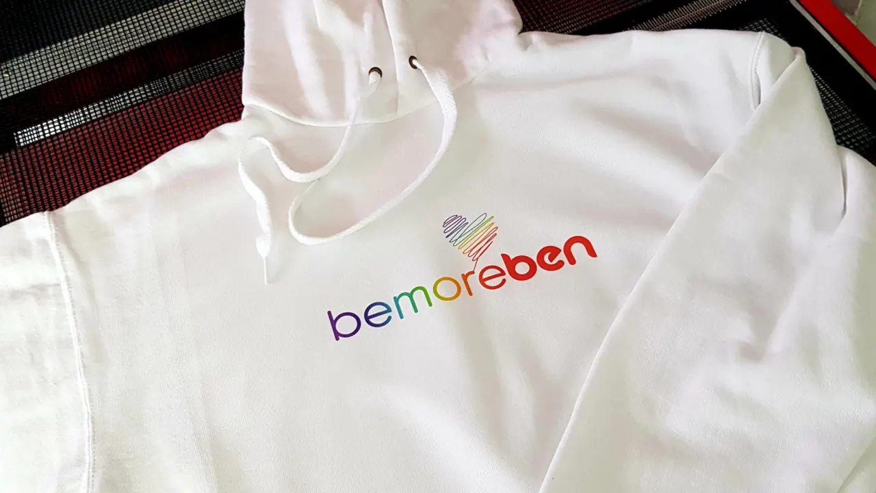 White hoodie printed with the rainbow bemoreben logo and a heart