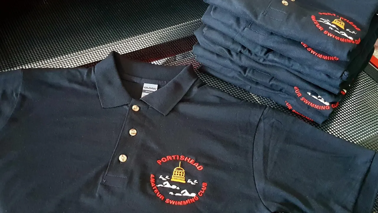 A stack of navy polo shirts embroidered with a Portishead swimming club badge