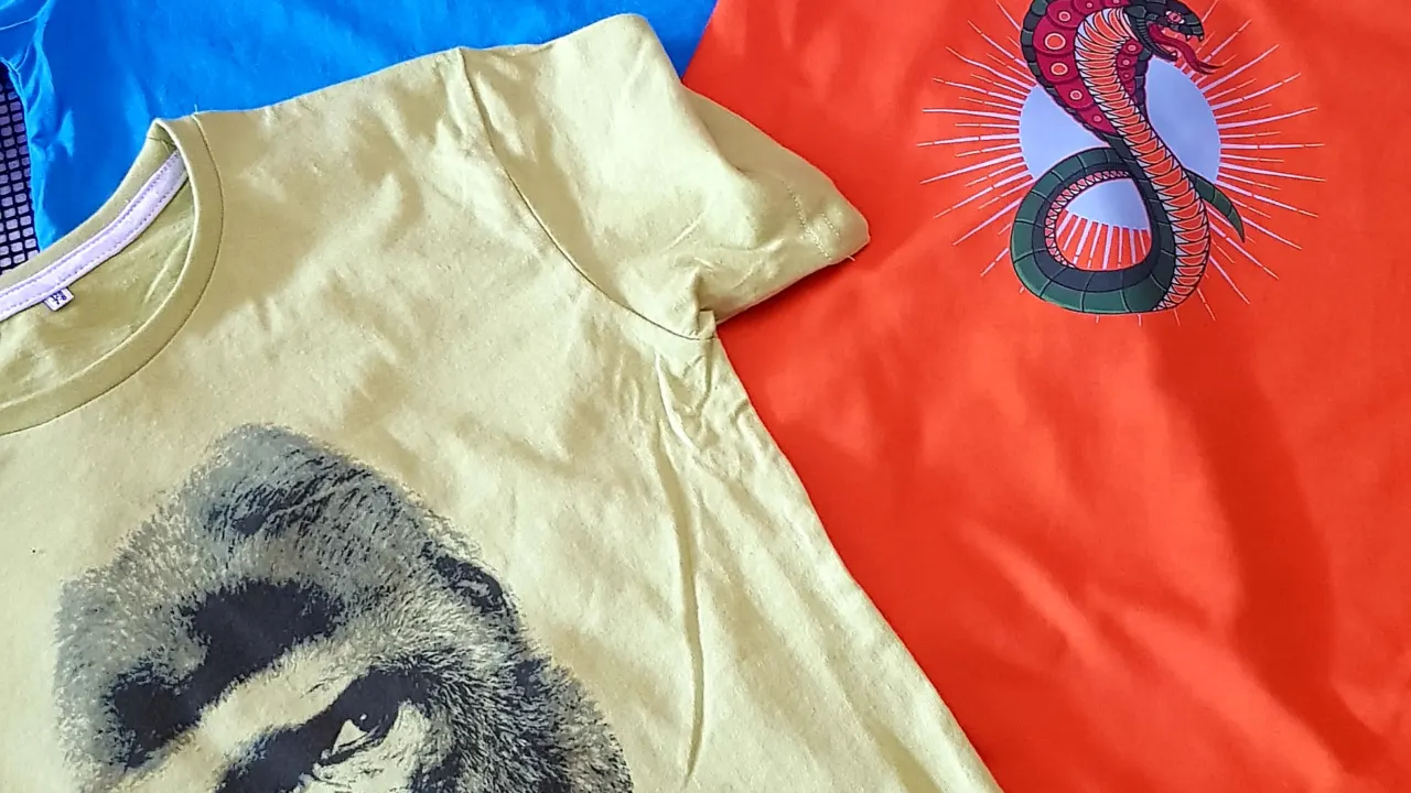 Three kids t-shirts in blue, orange and yellow printed with a slogan, a cobra and a gorilla
