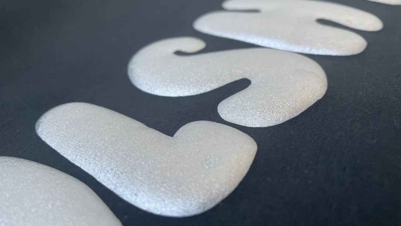 Close-up of raised white 3D puff lettering on a black garment