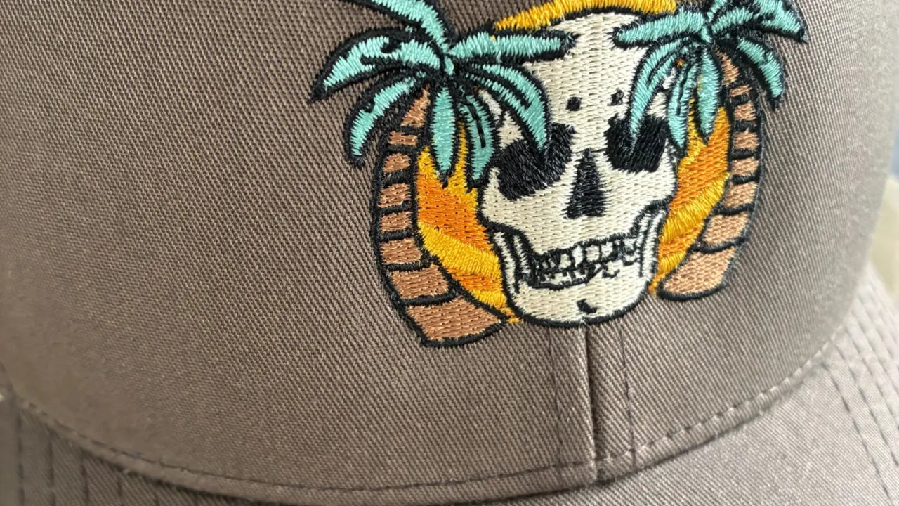 Close-up of a brown cap embroidered with a colourful palm tree and skull design