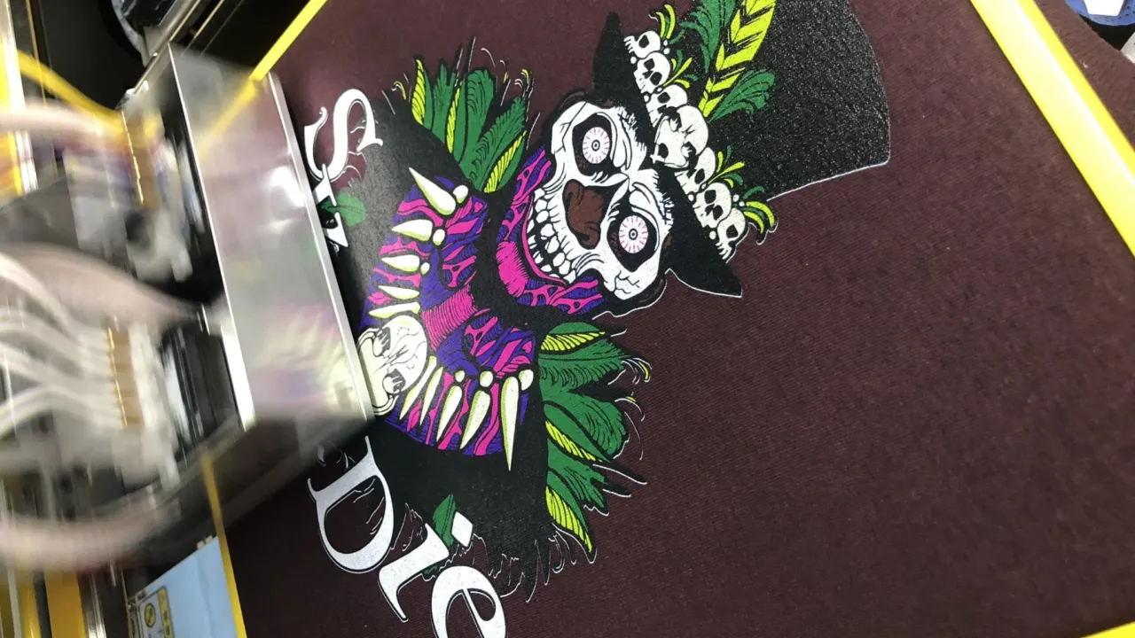 A direct to garment printer printing a colourful skull design onto a maroon t-shirt